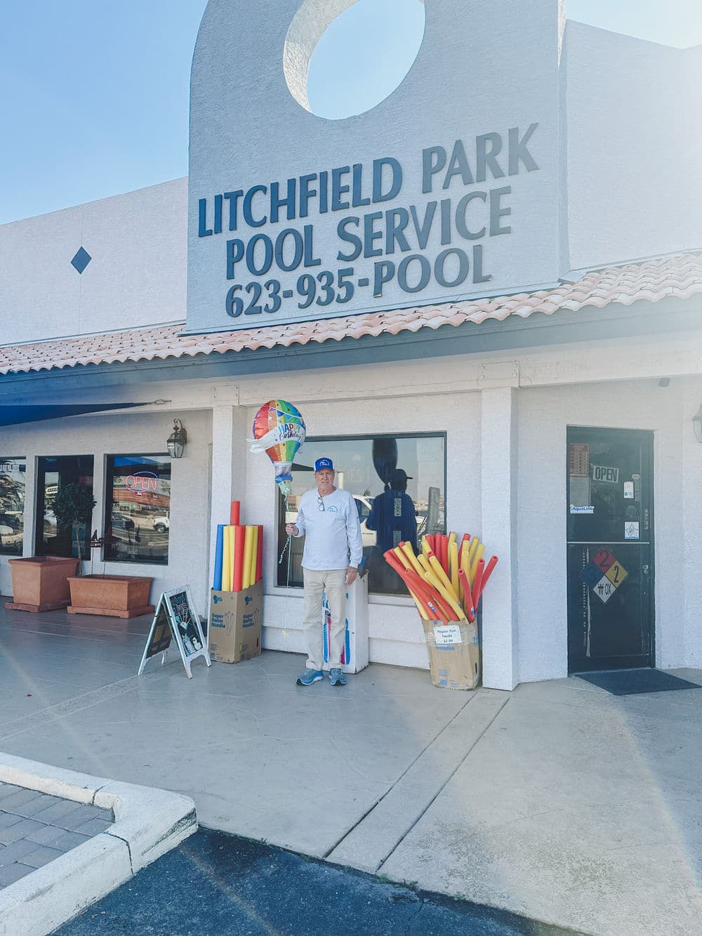 Litchfield Park Pool Service storefront with colorful pool toys and happy employee holding a balloon.