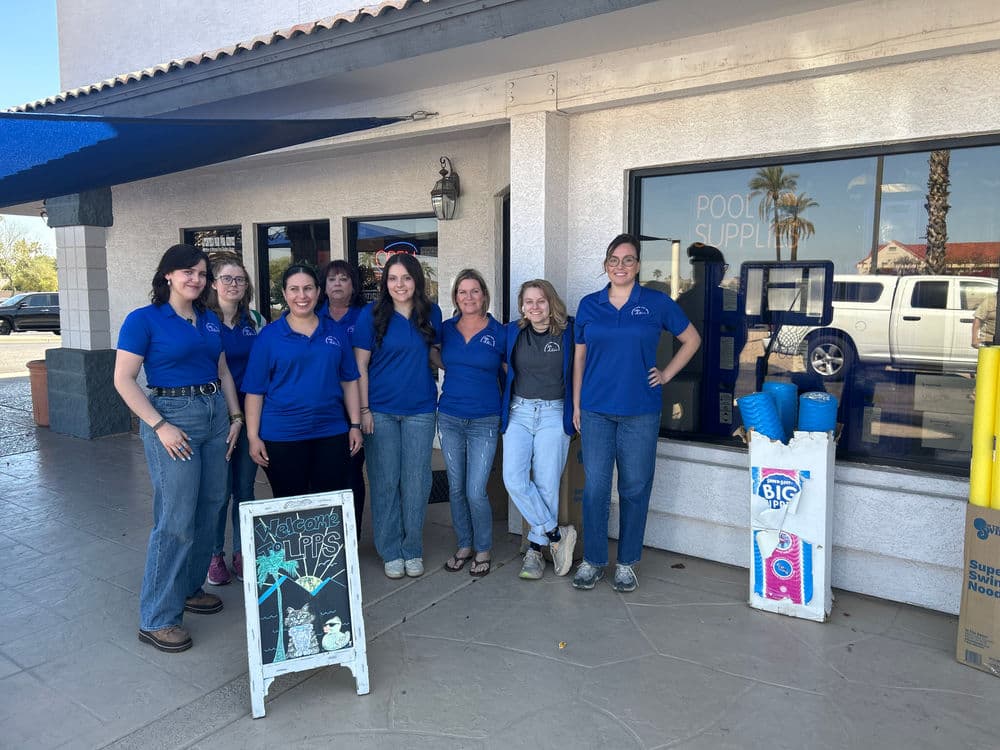 Group of women in blue shirts outside a pool supplies store, smiling together.